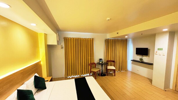 A hotel room with a bed, a desk, two chairs, a television, and a small table. - Foura Suites Makati (Makati)