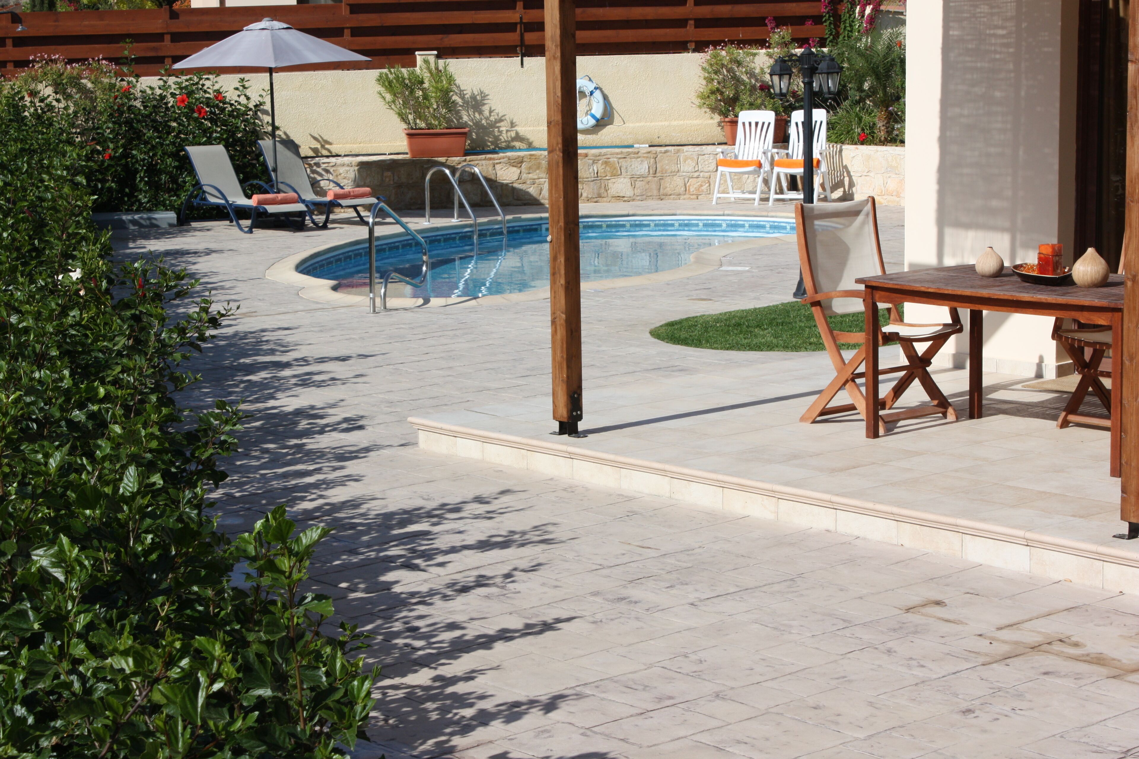 A backyard with a swimming pool, lounge chairs, a wooden table, and potted plants.