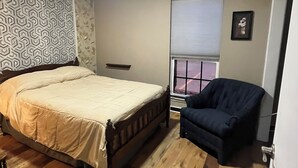 A bedroom with a bed, a chair, a window with blinds, and a patterned wall. - Quiet ground floor 2 bedroom- unwind in private. (Garland)