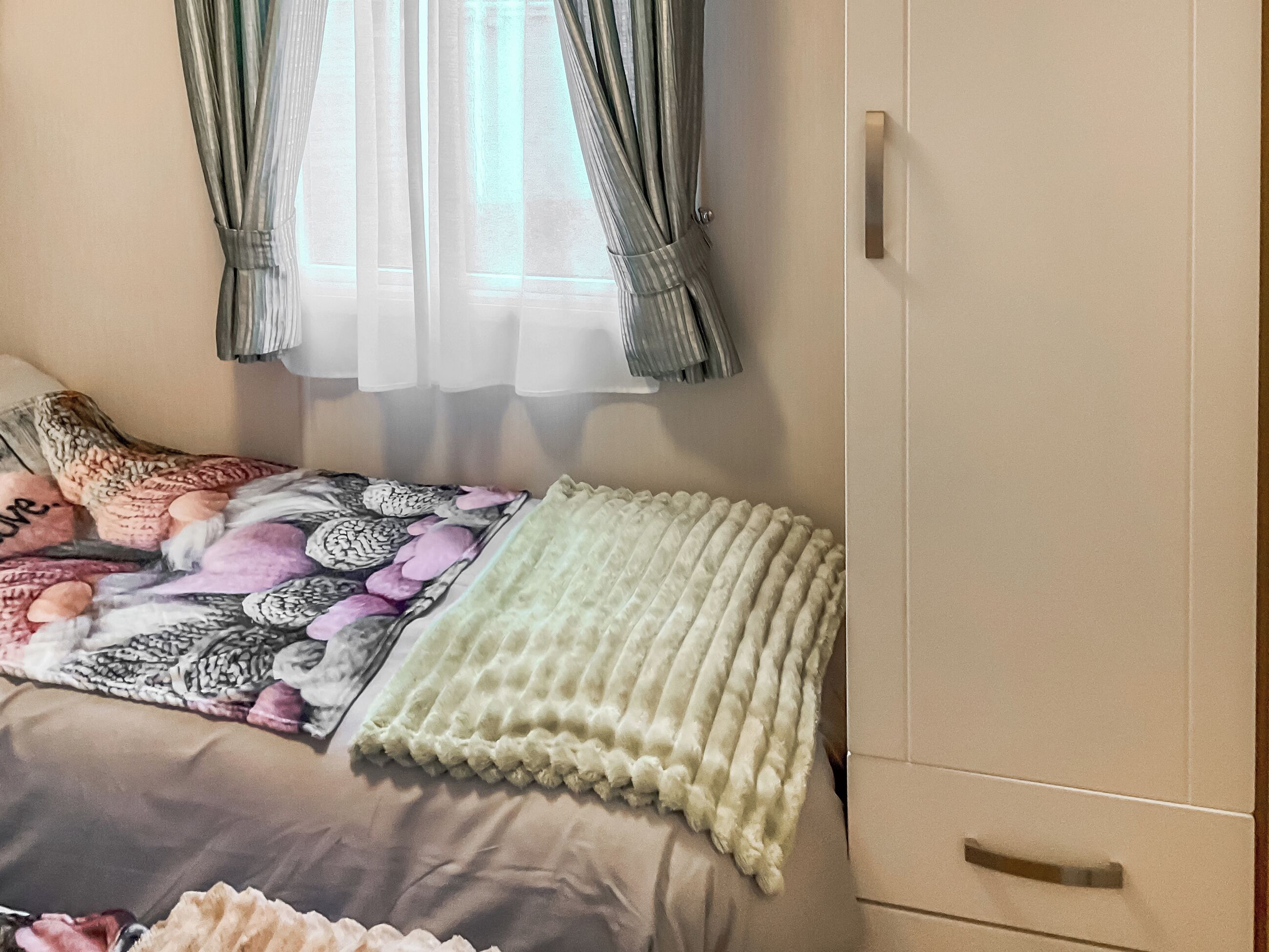 A bed with a patterned blanket, a pillow, and a light-colored throw.