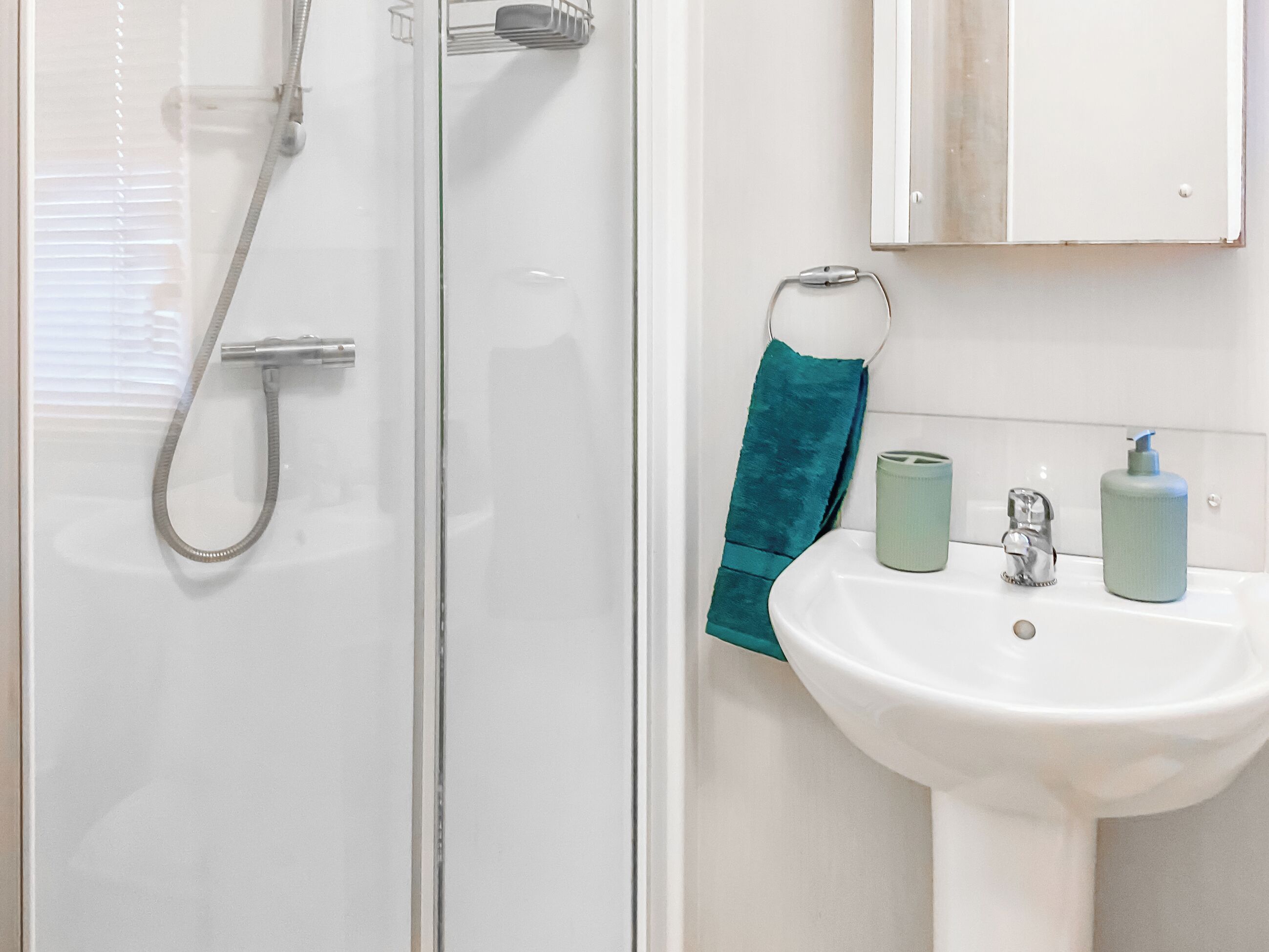 Een badkamer met een glazen douchecabine, een witte wastafel met spiegel erboven en een blauwgroene handdoek aan de muur.