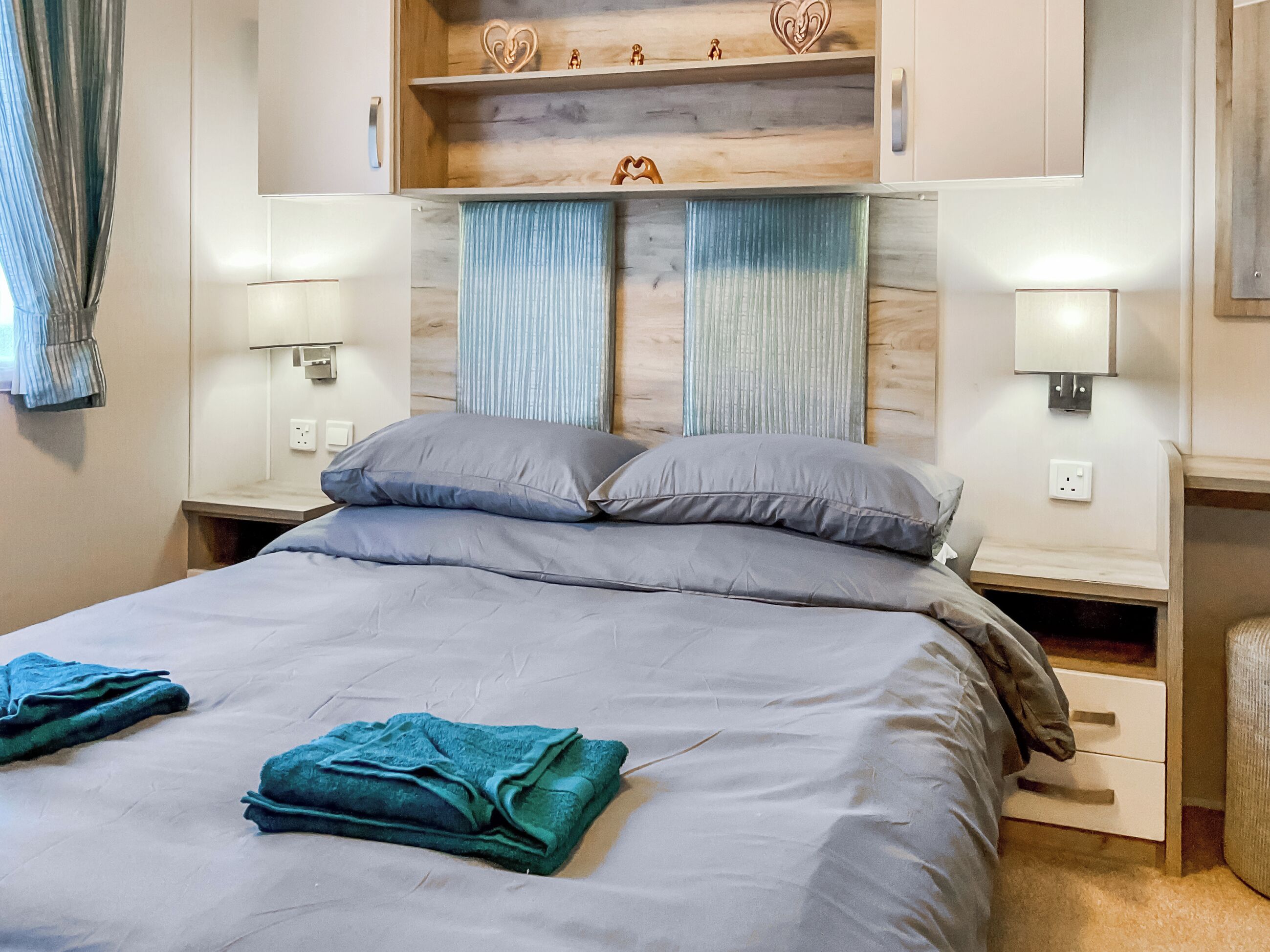 A neatly made bed with pillows, a bedside table, and a wall-mounted shelf with decorative items.
