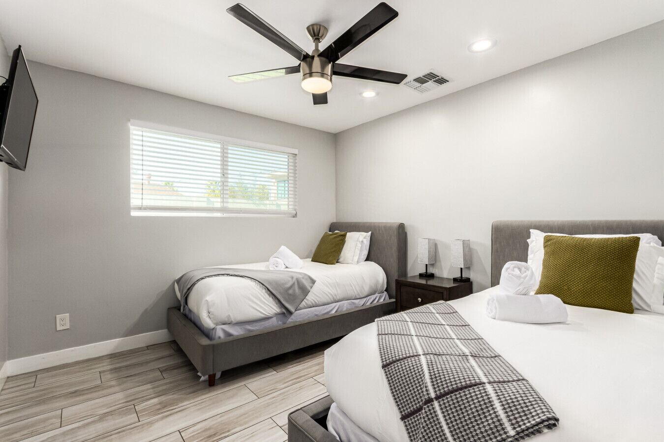 A modern hotel room with a bed, bedside tables, a ceiling fan, and a window with blinds.
