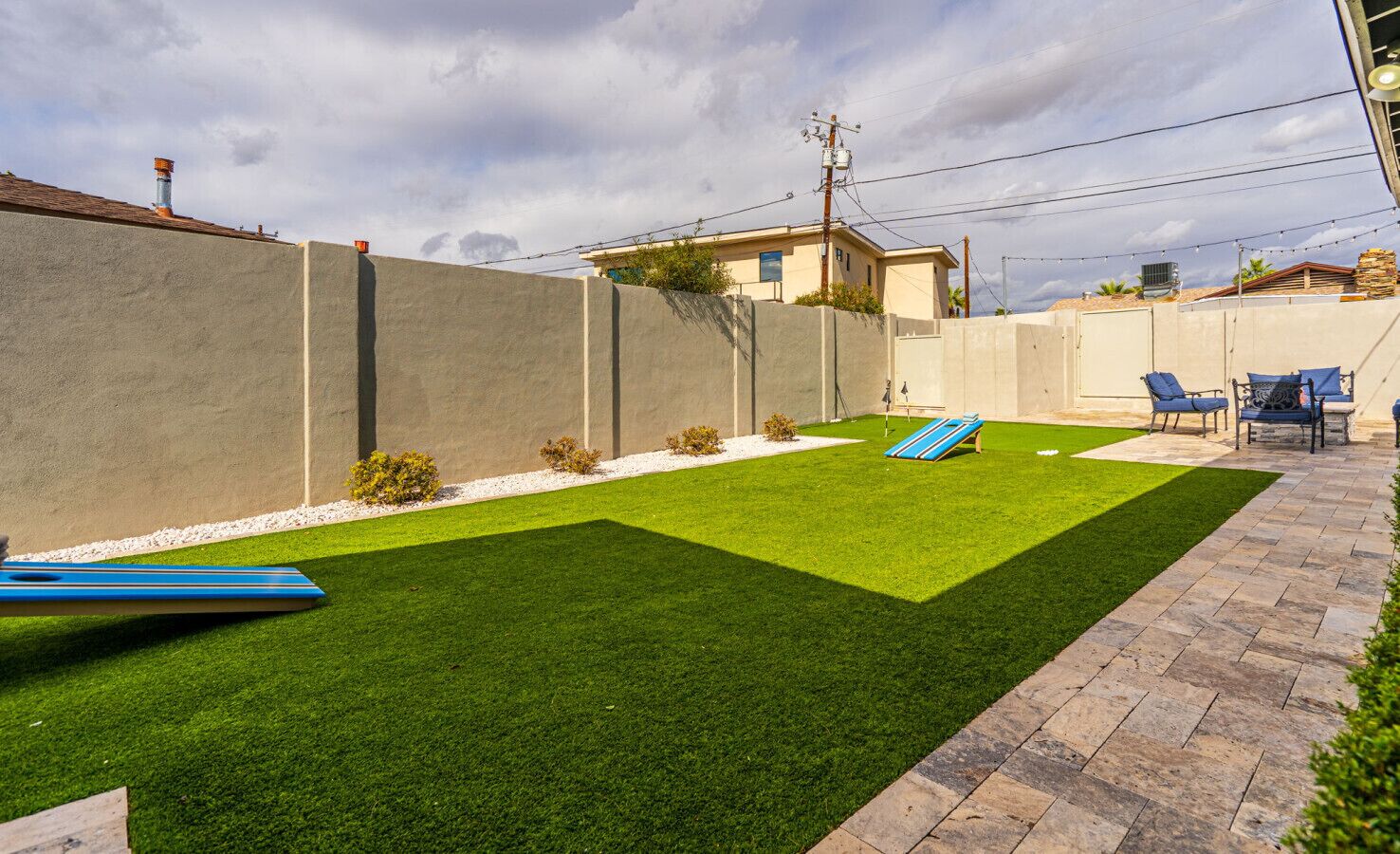 A backyard with artificial grass, a pool, and a patio area with chairs.