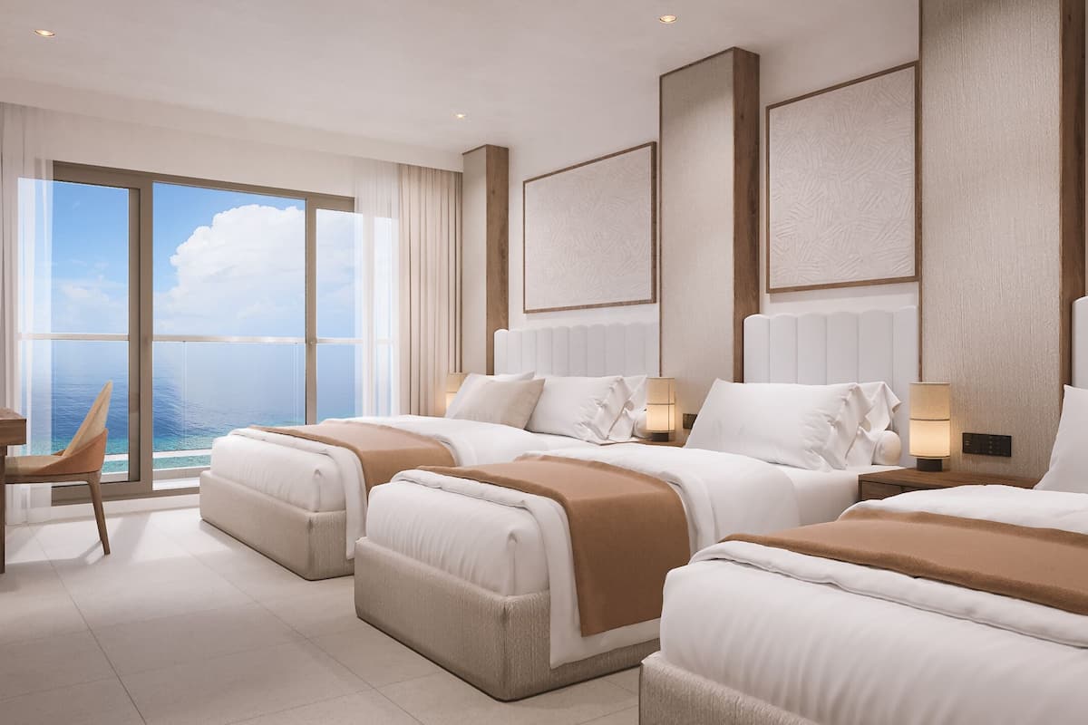 Une chambre d’hôtel moderne dotée d’une grande fenêtre donnant sur la mer, d’un lit avec une tête de lit, d’une table de chevet et d’une chaise.