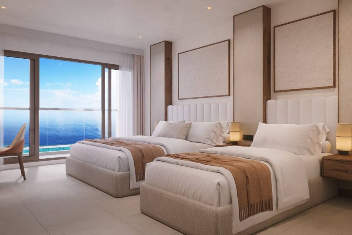 Une chambre d’hôtel moderne avec deux lits, de grandes fenêtres, une vue sur l’océan et une table de chevet en bois avec une lampe.