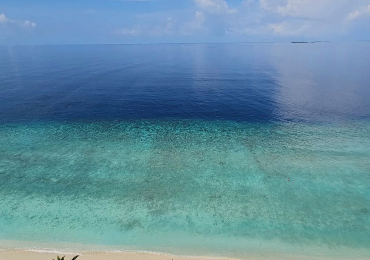 Ein Strand mit klarem türkisblauem Wasser und einem Schiffen im Hintergrund.