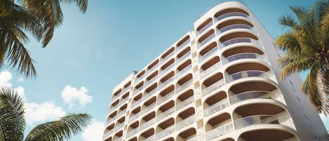 Un hotel de varios pisos con una fachada curva, numerosos balcones y palmeras en primer plano.