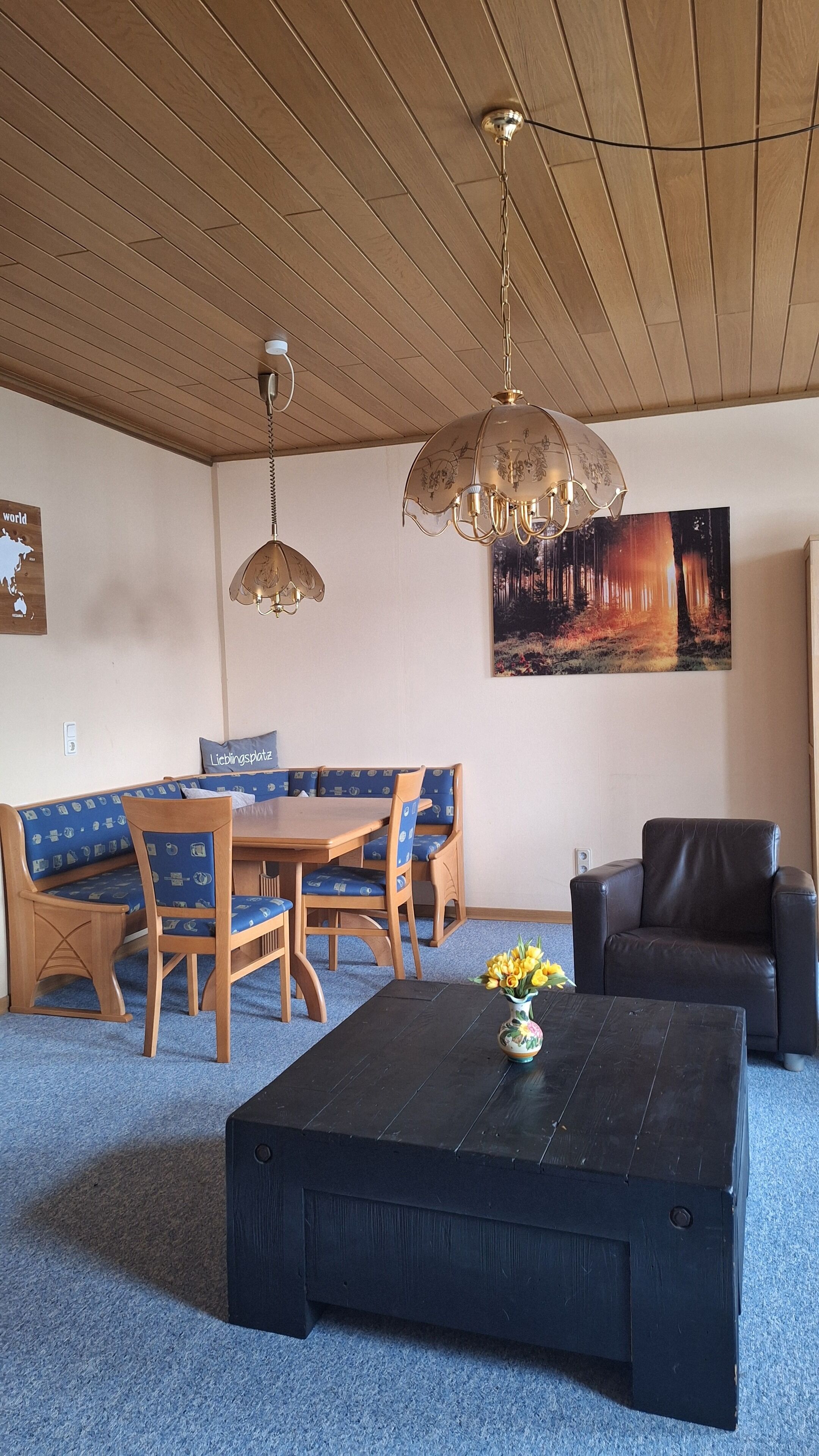 A living room with a wooden ceiling, a black coffee table, a sofa, and a dining table with chairs.