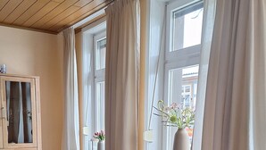 A living room with a black sofa, a wooden cabinet, and a window with curtains. - A cozy vacation apartment in a charming former hotel. (Sankt Andreasberg)