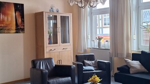 A modern living room with a wooden ceiling, a chandelier, a cabinet, and a sofa. - A cozy vacation apartment in a charming former hotel. (Sankt Andreasberg)