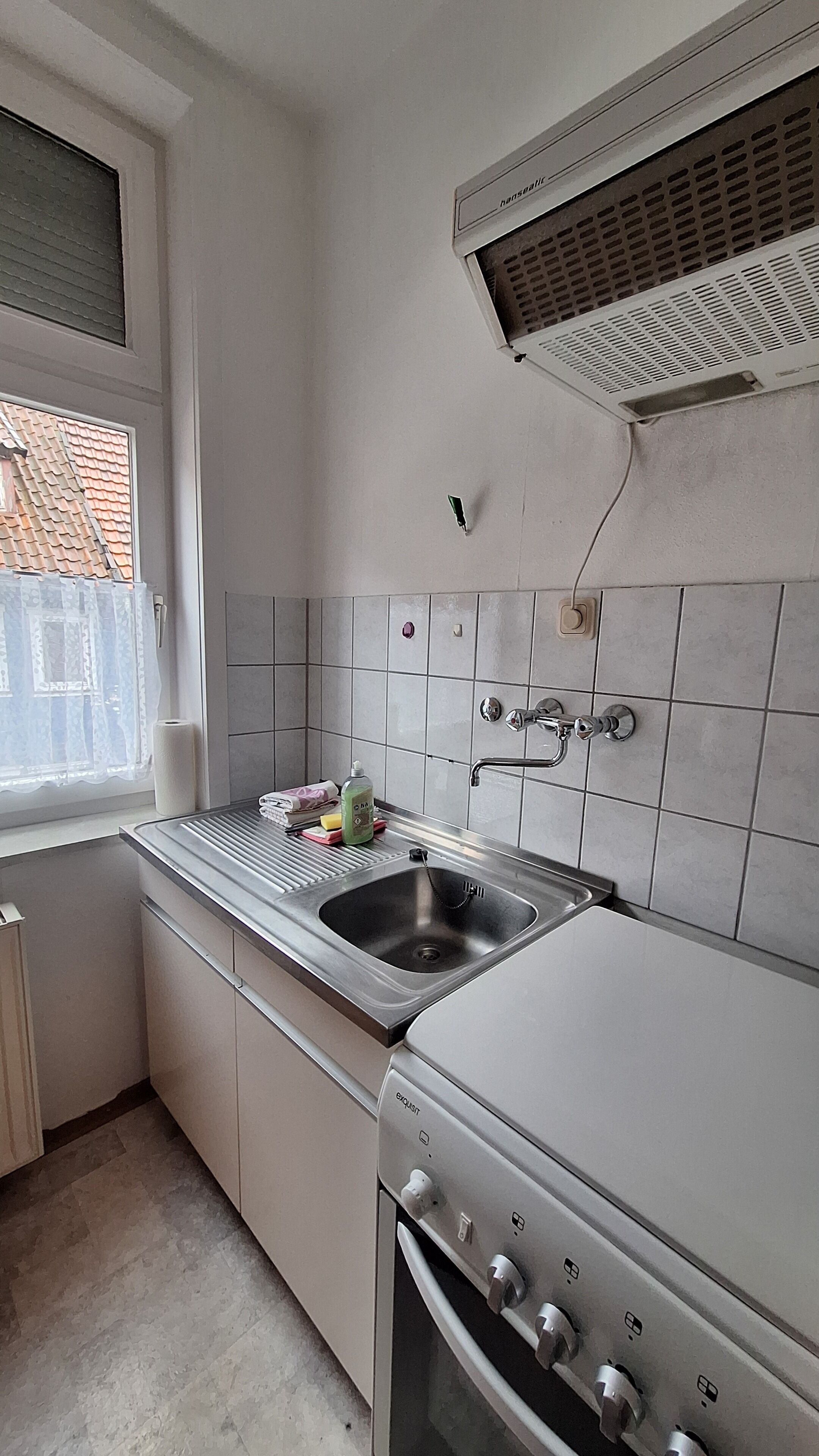 A kitchen with a stainless steel sink, a built-in oven, and a window with a view of a tiled roof.