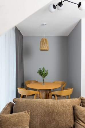 A dining area with a round table, chairs, a hanging woven light fixture, and a vase with greenery.