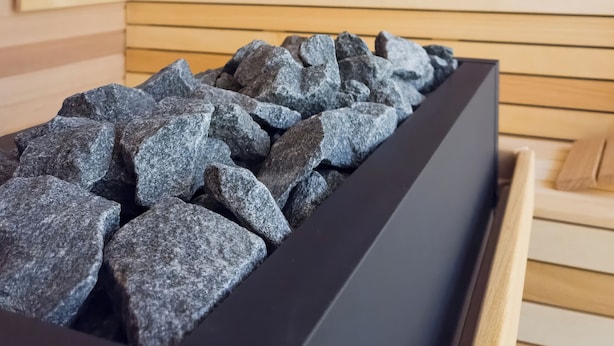 A sauna with wooden walls and a black container filled with rocks. - Baltic Season Spa Apartments (Grzybowo)