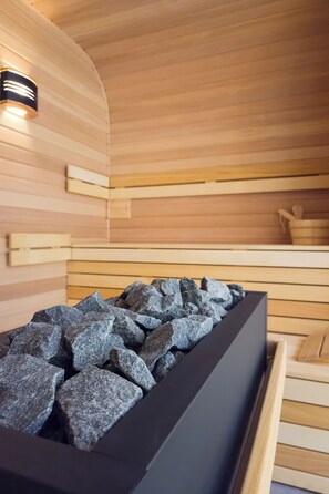 A sauna with wooden walls and a black container filled with rocks.
