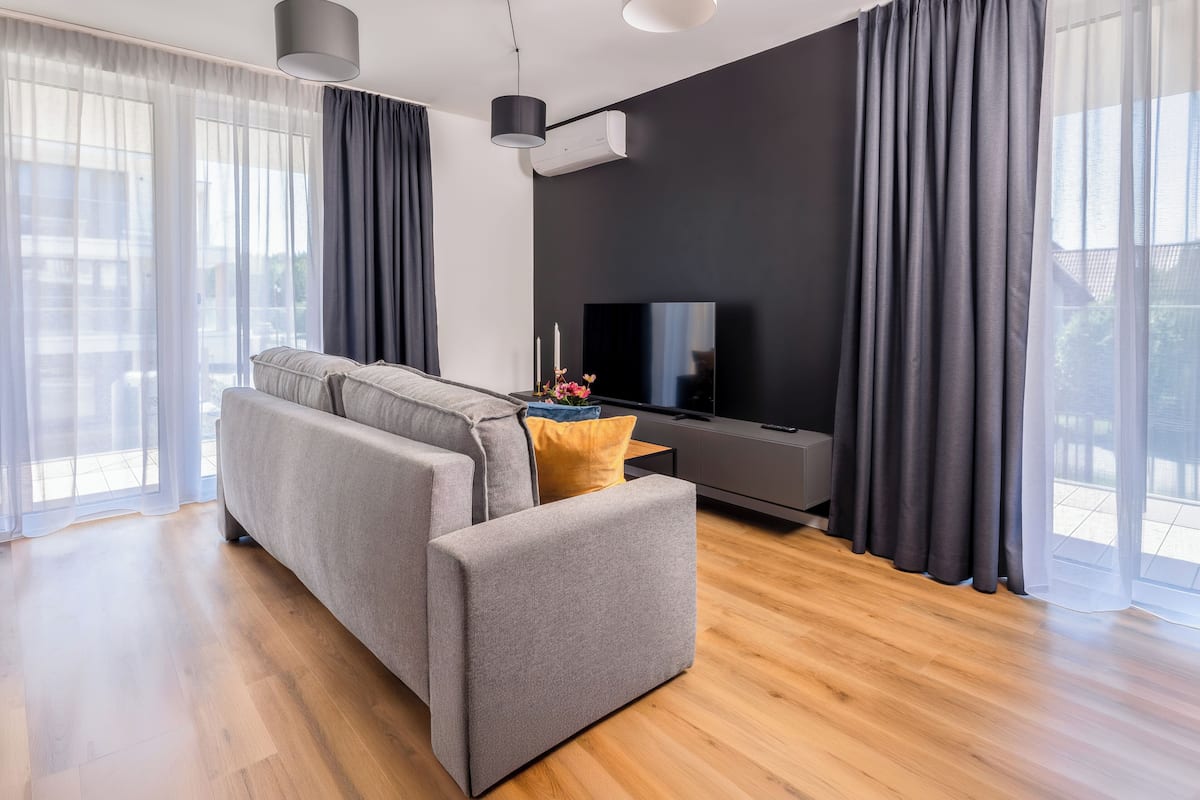 Ein modernes Wohnzimmer mit einer Couch, einem Flachbildfernseher und einem großen Fenster mit Vorhängen.
