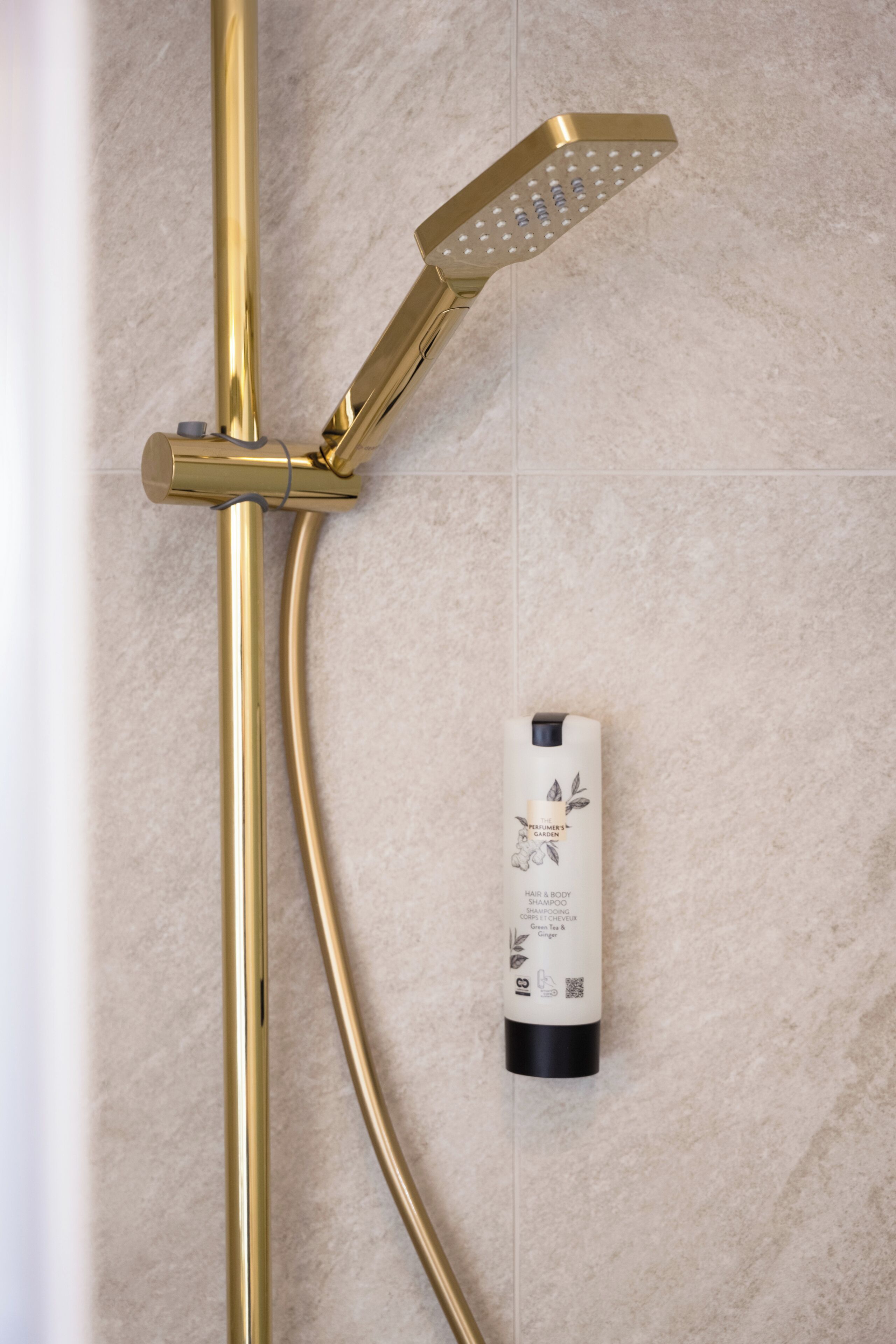 A bathroom with a gold showerhead and a bottle of shampoo.