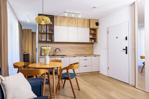 A modern kitchen with wooden cabinets, a dining table with chairs, and a hanging light fixture. - Baltic Season Spa Apartments (Grzybowo)