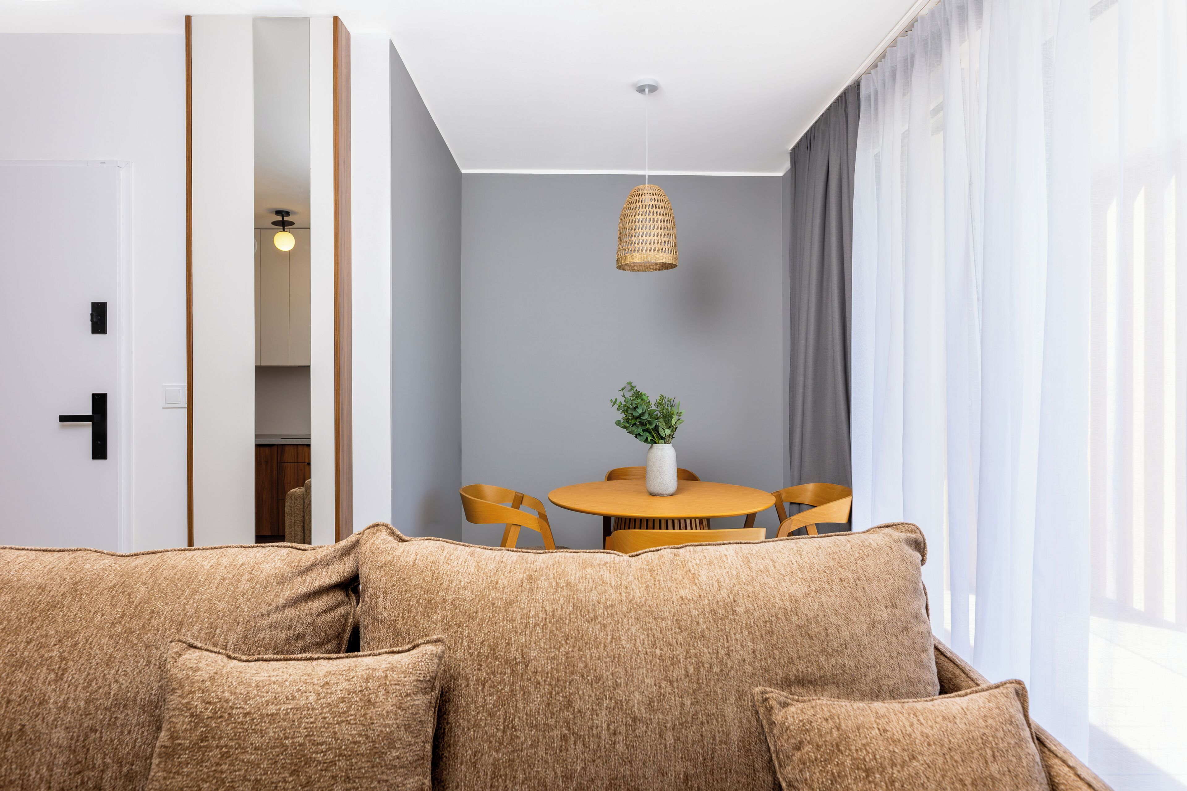 A modern living room with a sofa, a dining table with chairs, and a hanging light fixture.