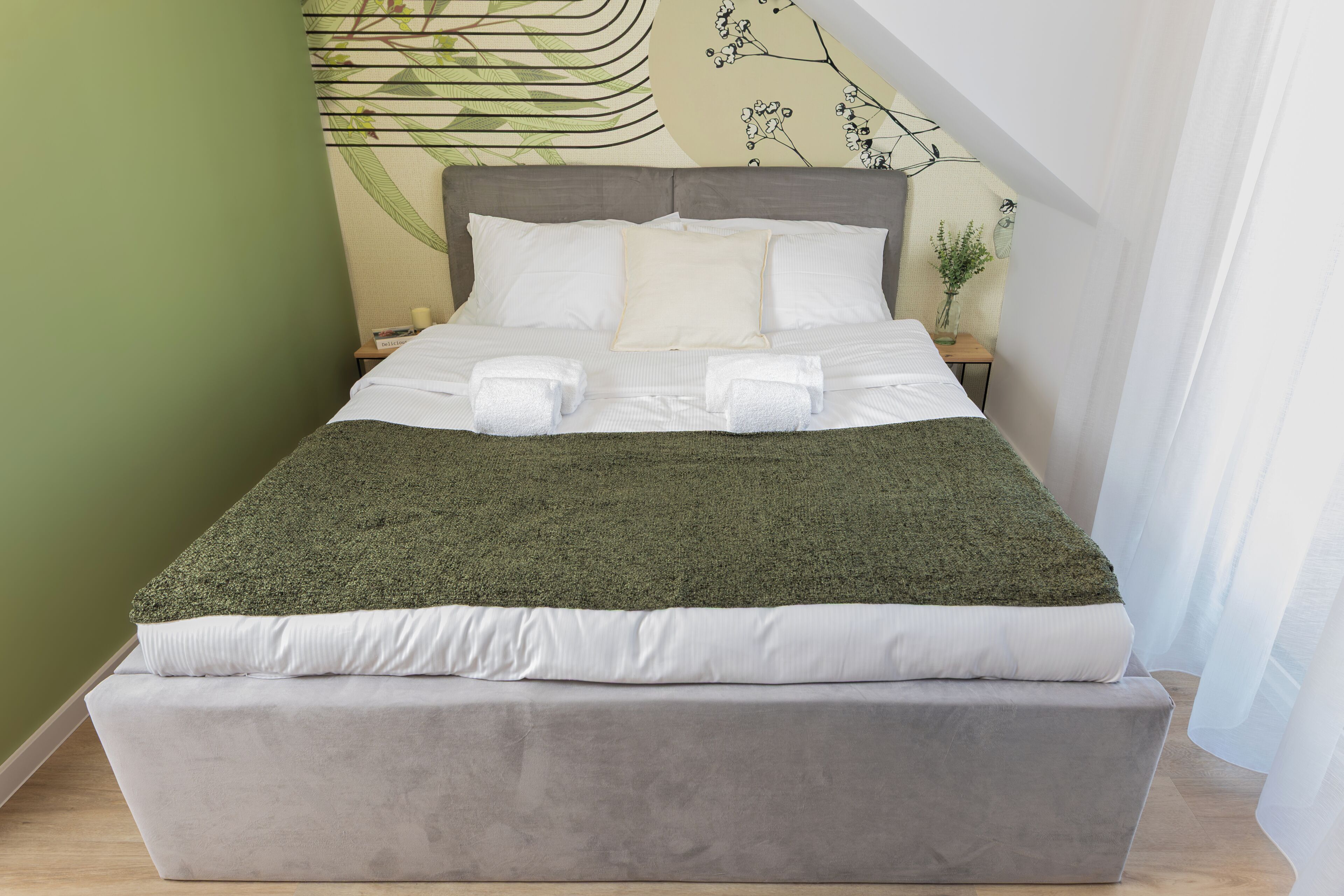 A bed with a grey headboard, white bedding, and a green throw blanket.