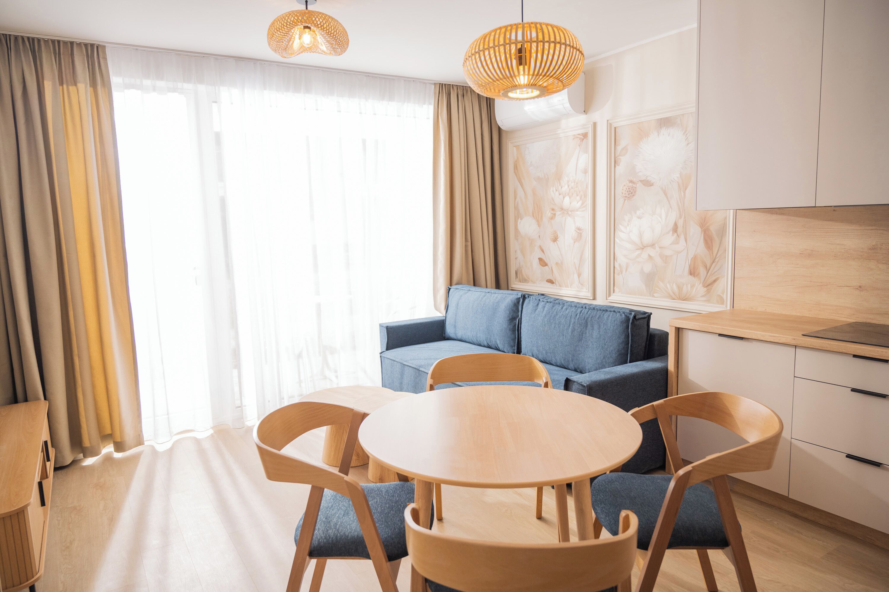 Quarto moderno com mesa de madeira redonda, sofá azul e cadeiras de madeira.