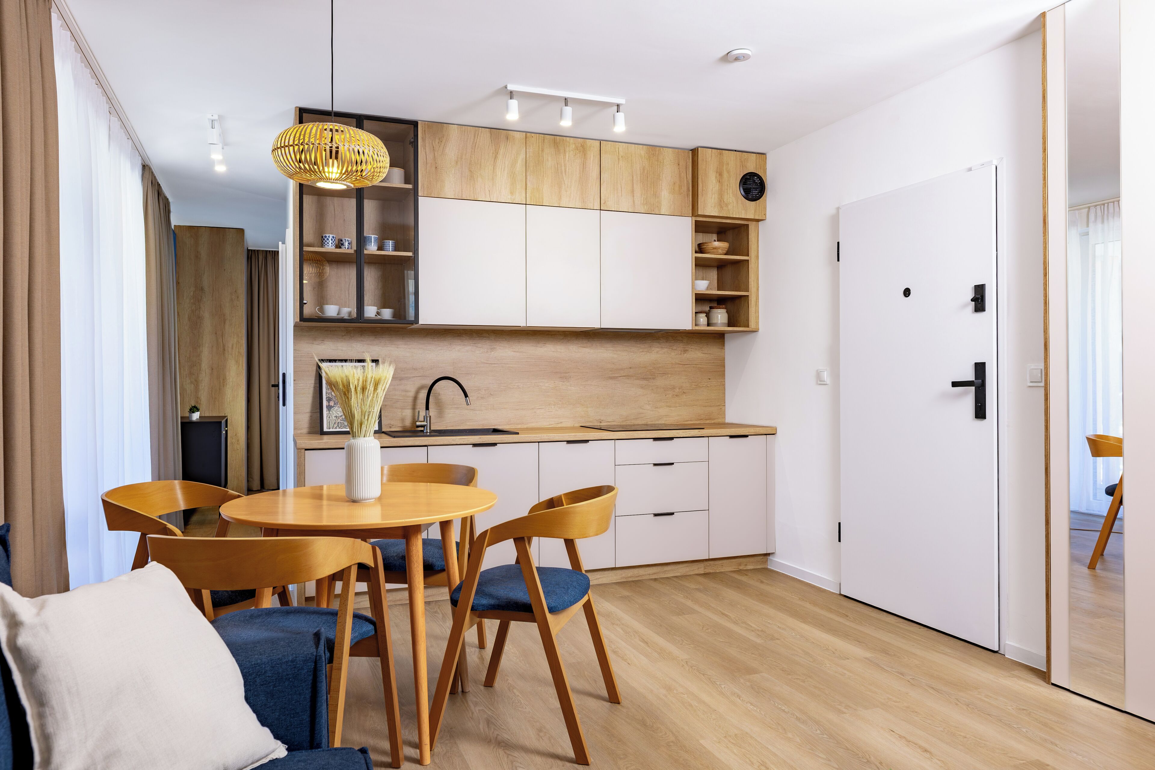 Eine moderne Küche mit Holzschränken, ein Essbereich mit rundem Tisch und Stühlen sowie eine weiße Tür.