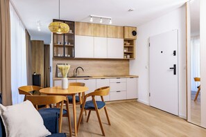 A modern kitchen with wooden cabinets, a dining area with a round table and chairs, and a white door. - Baltic Season Spa Apartments (Grzybowo)