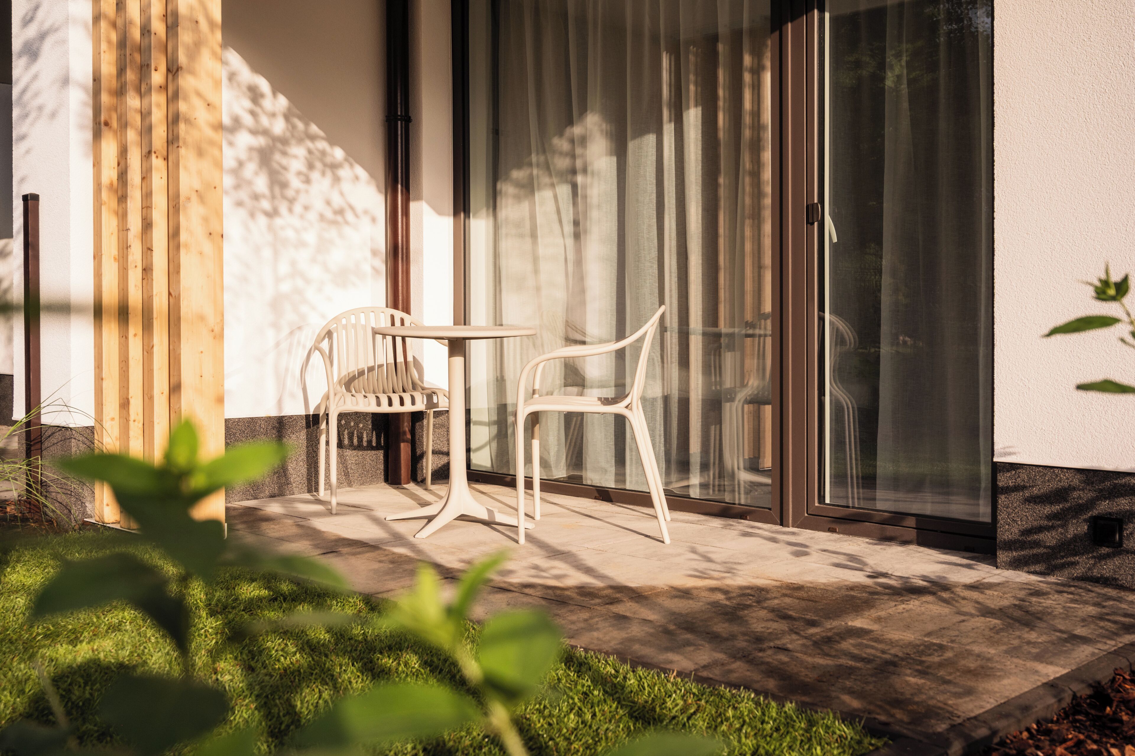 A patio with two white chairs and a table, a wooden post, and a glass door.