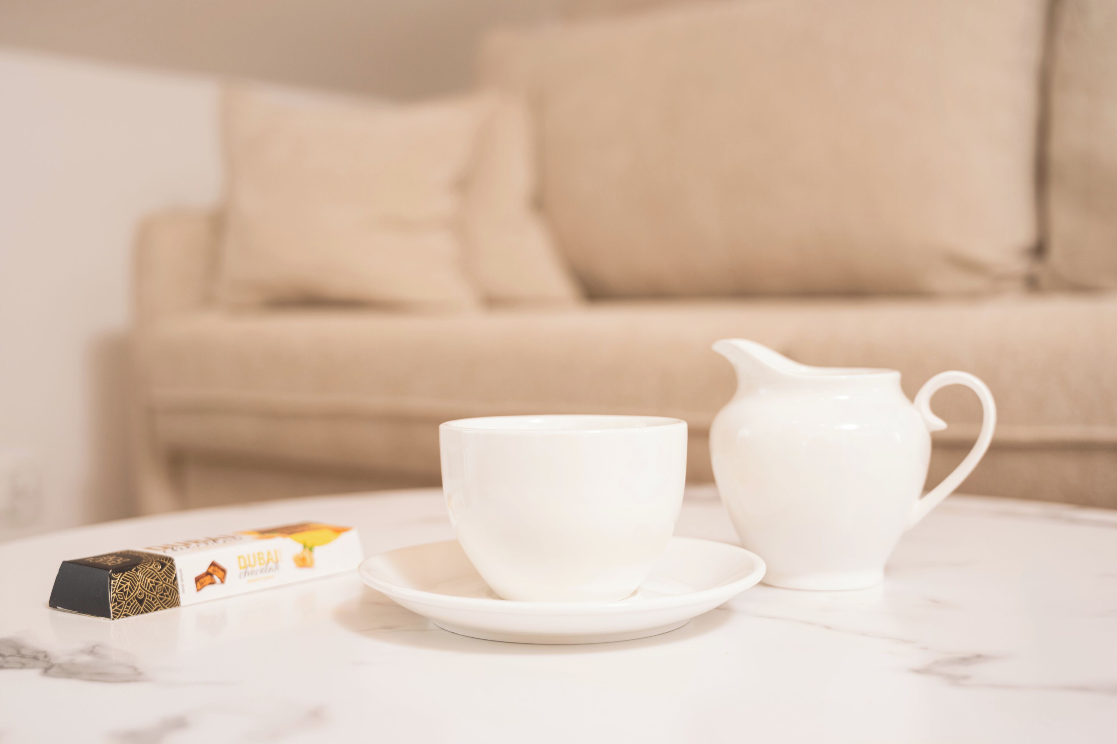 A white teapot and cup on a white table with a box of tea.