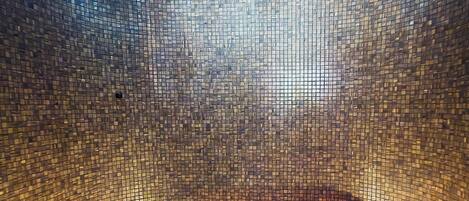 A circular hot tub with mosaic tile walls and ceiling, surrounded by recessed lighting.