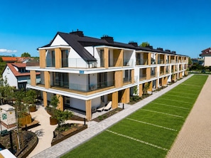 A modern multi-story residential building with balconies, a well-maintained lawn, and a clear sky.