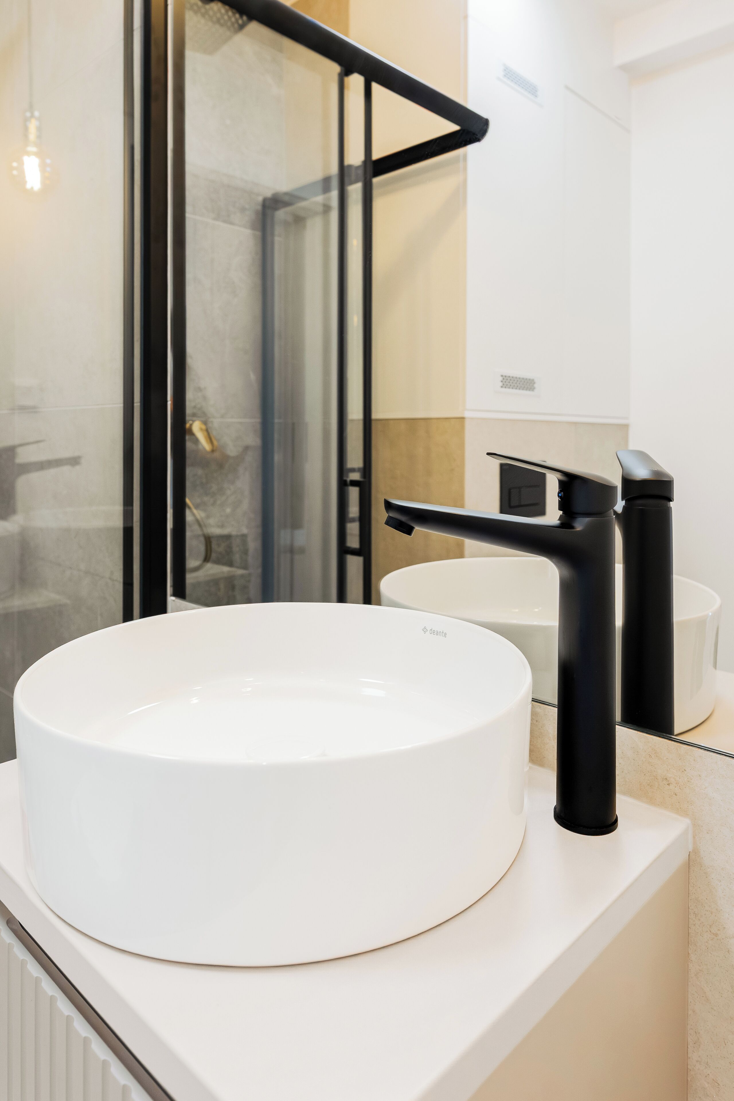 A modern bathroom with a white sink, black faucet, and a glass shower enclosure.