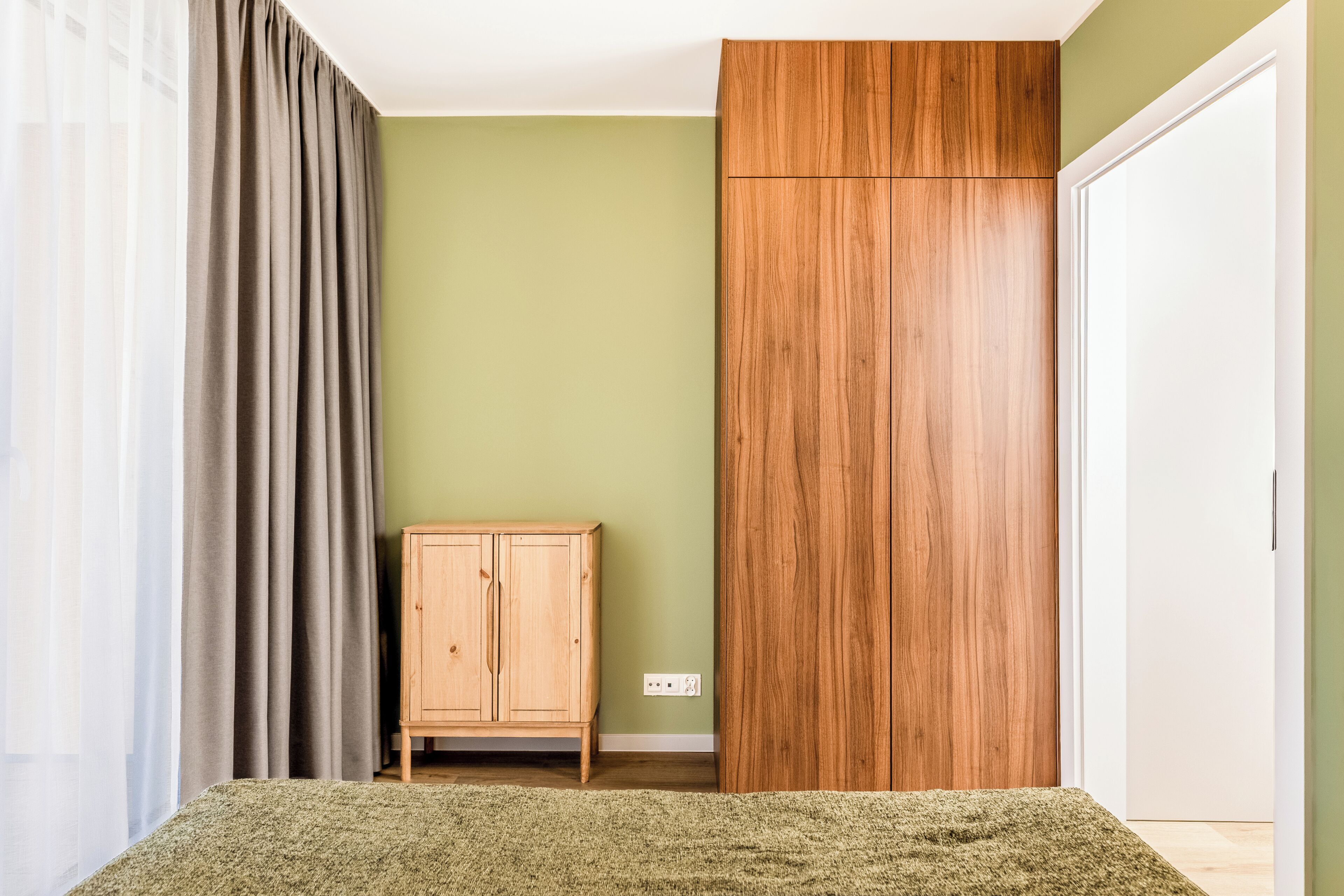 A room with a green wall, a wooden wardrobe, a wooden cabinet, and a carpeted floor.