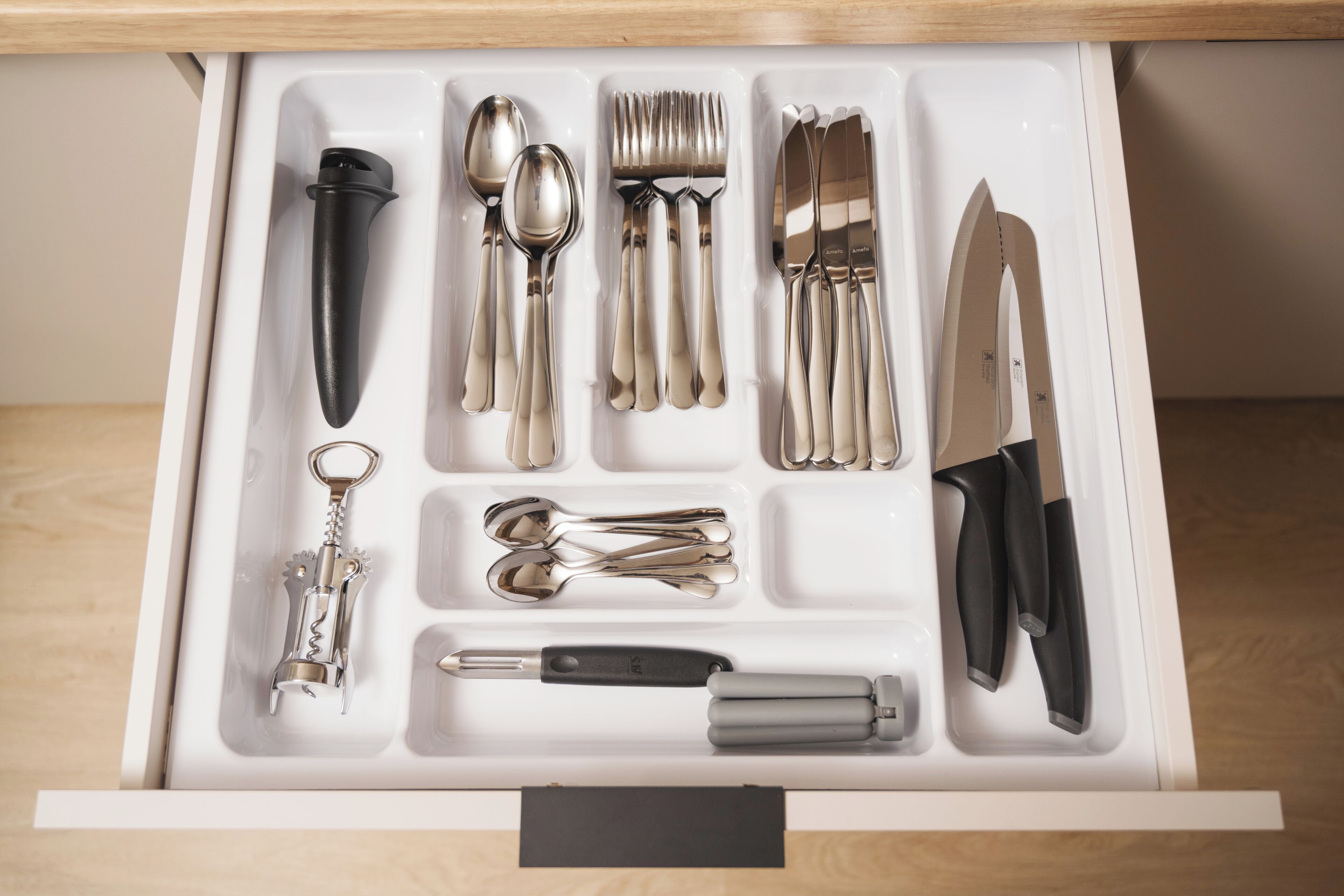 A drawer with various utensils and tools, including spoons, forks, knives, and a corkscrew.