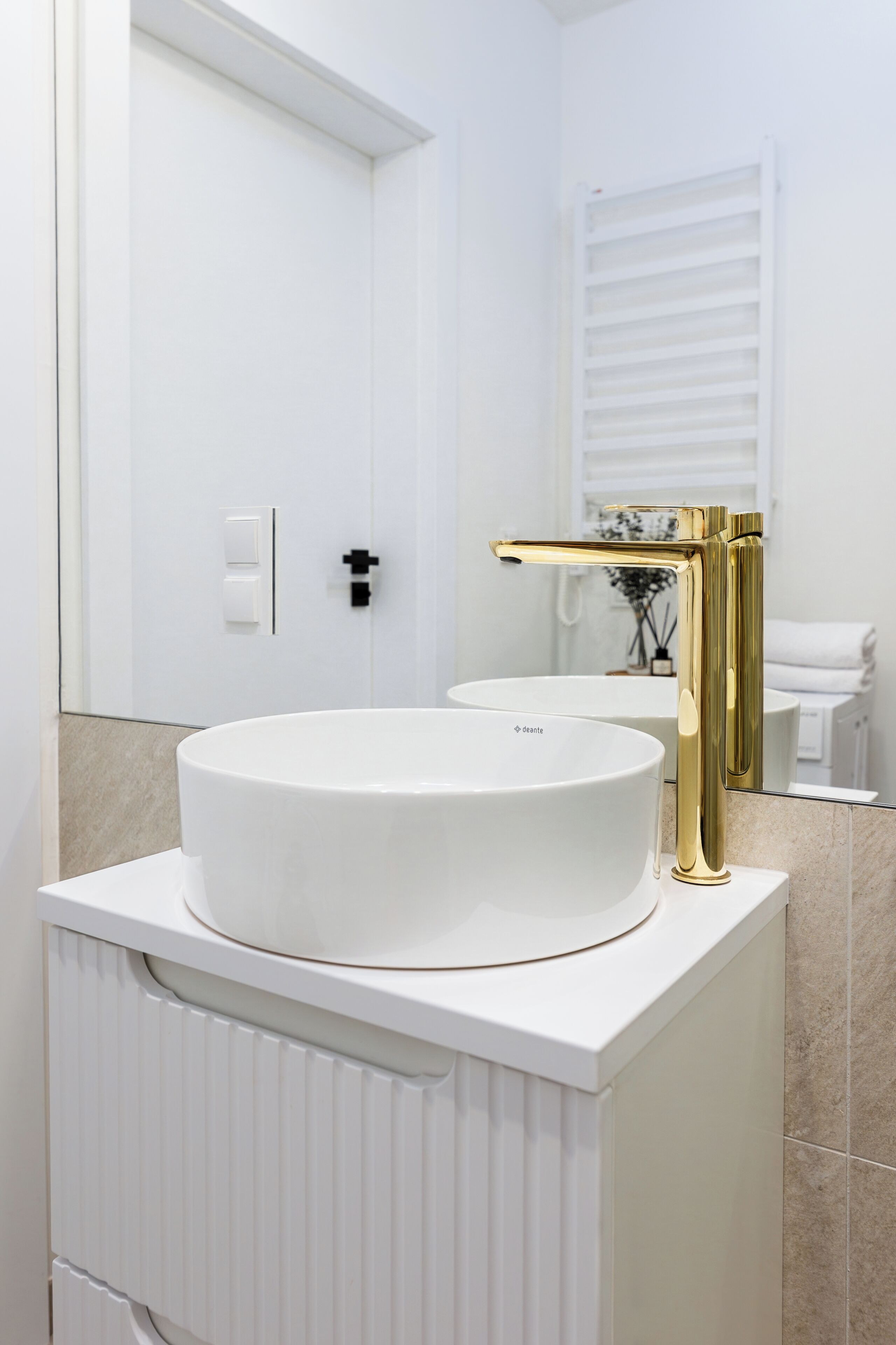 Un baño moderno con un lavamanos blanco, grifo dorado y un espejo grande.