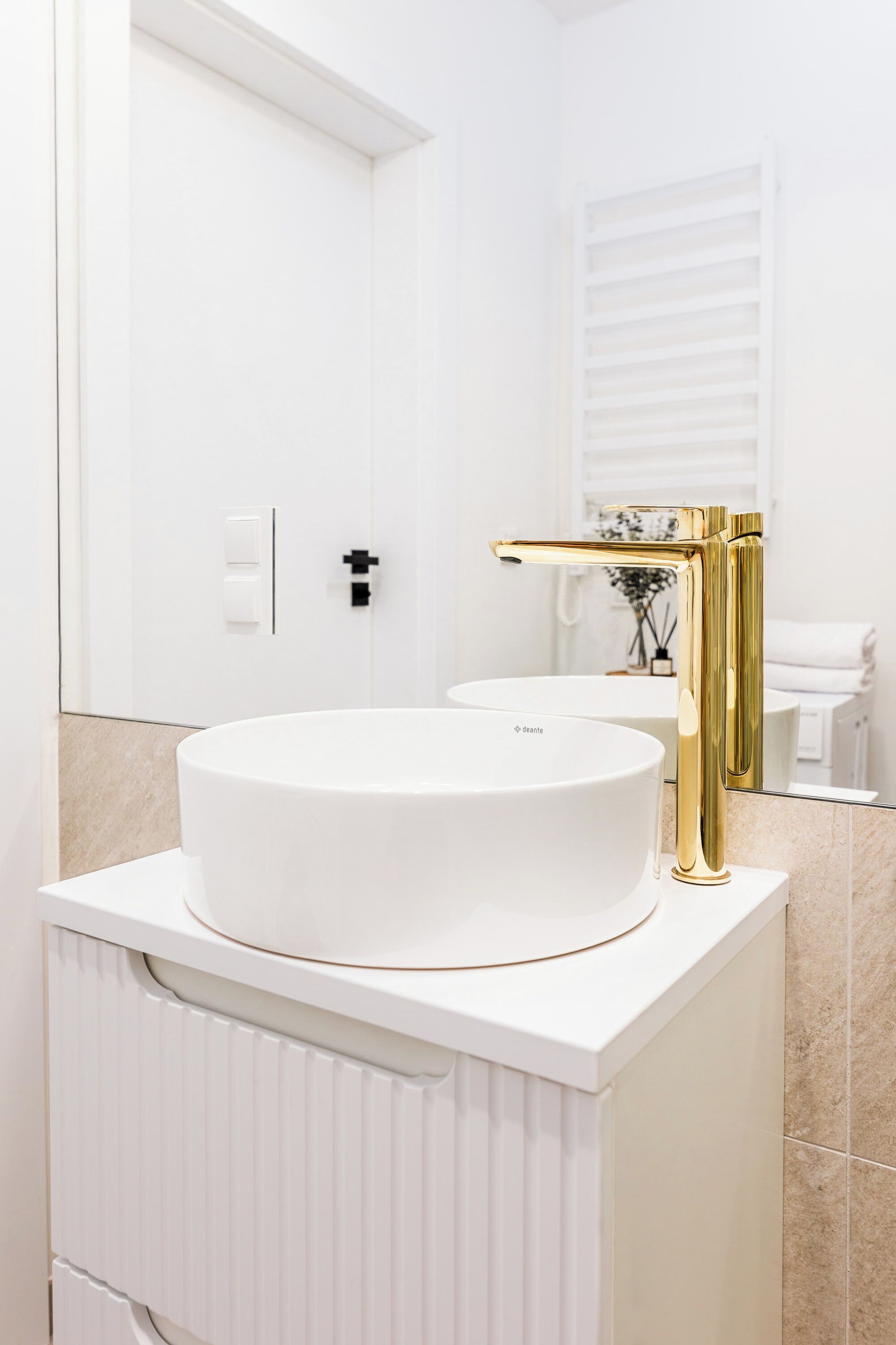 Une salle de bain moderne avec un lavabo blanc, un robinet doré et un grand miroir.