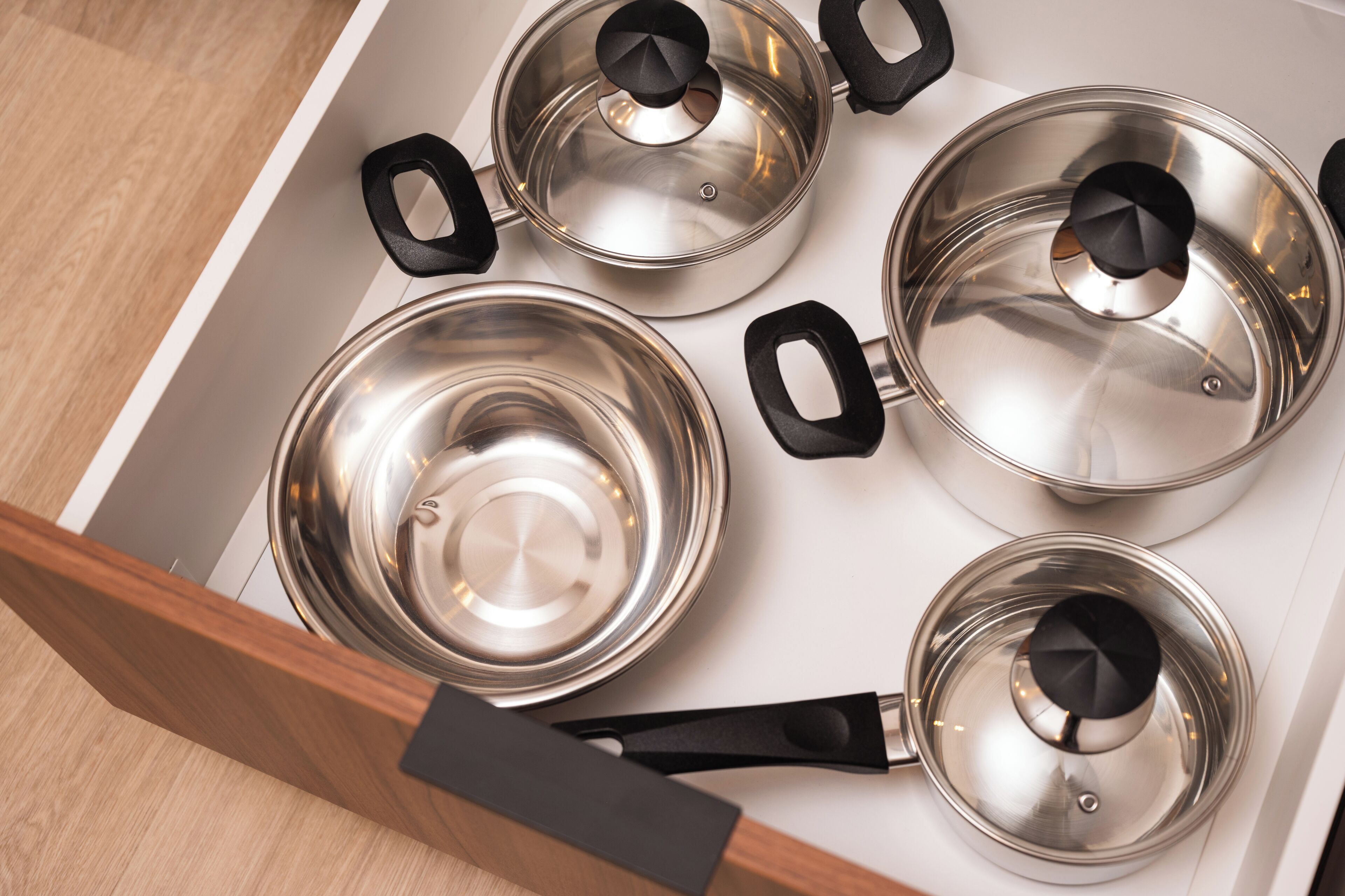 A kitchen with four stainless steel pots with lids and black handles.