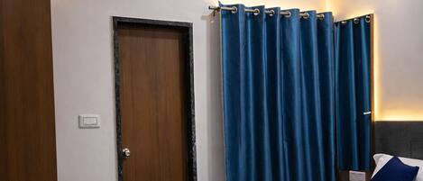 A bedroom with a bed, a ceiling fan, an air conditioning unit, a door, and blue curtains.