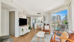 A modern apartment with a living room, dining area, and kitchen. It features a large window with a city view, a flat-screen TV, and a cozy seating area. - Twin Towns 233 - Central Coolangatta / Tweed Heads - Min. 3 Night Stays - Linen Provided (Tweed Heads)