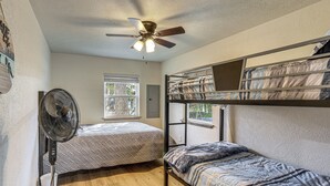 A room with two bunk beds, a standing fan, a ceiling fan, and a window with a view of trees. - Fish Sam Rayburn! Secluded Cabin w/ Deck & Grill (Brookeland)