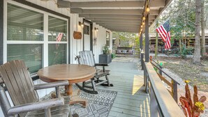 A covered outdoor patio with a wooden table and chairs, an American flag, and a view of a garden. - Fish Sam Rayburn! Secluded Cabin w/ Deck & Grill (Brookeland)