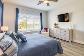 Une chambre à coucher avec un lit, une commode, une télévision et une fenêtre avec des rideaux.