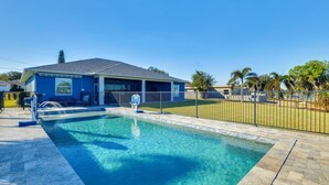 A swimming pool area with a blue building, a fenced patio, and a clear sky. - Poolside Paradise & Boat Dock! Haven on Lake Clay (Lake Placid)