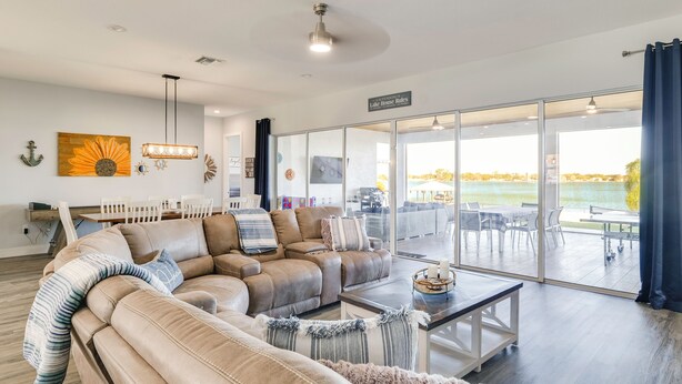 A spacious living room with a large sectional sofa, a dining area, and a view of a lake through large sliding glass doors. - Poolside Paradise & Boat Dock! Haven on Lake Clay (Lake Placid)