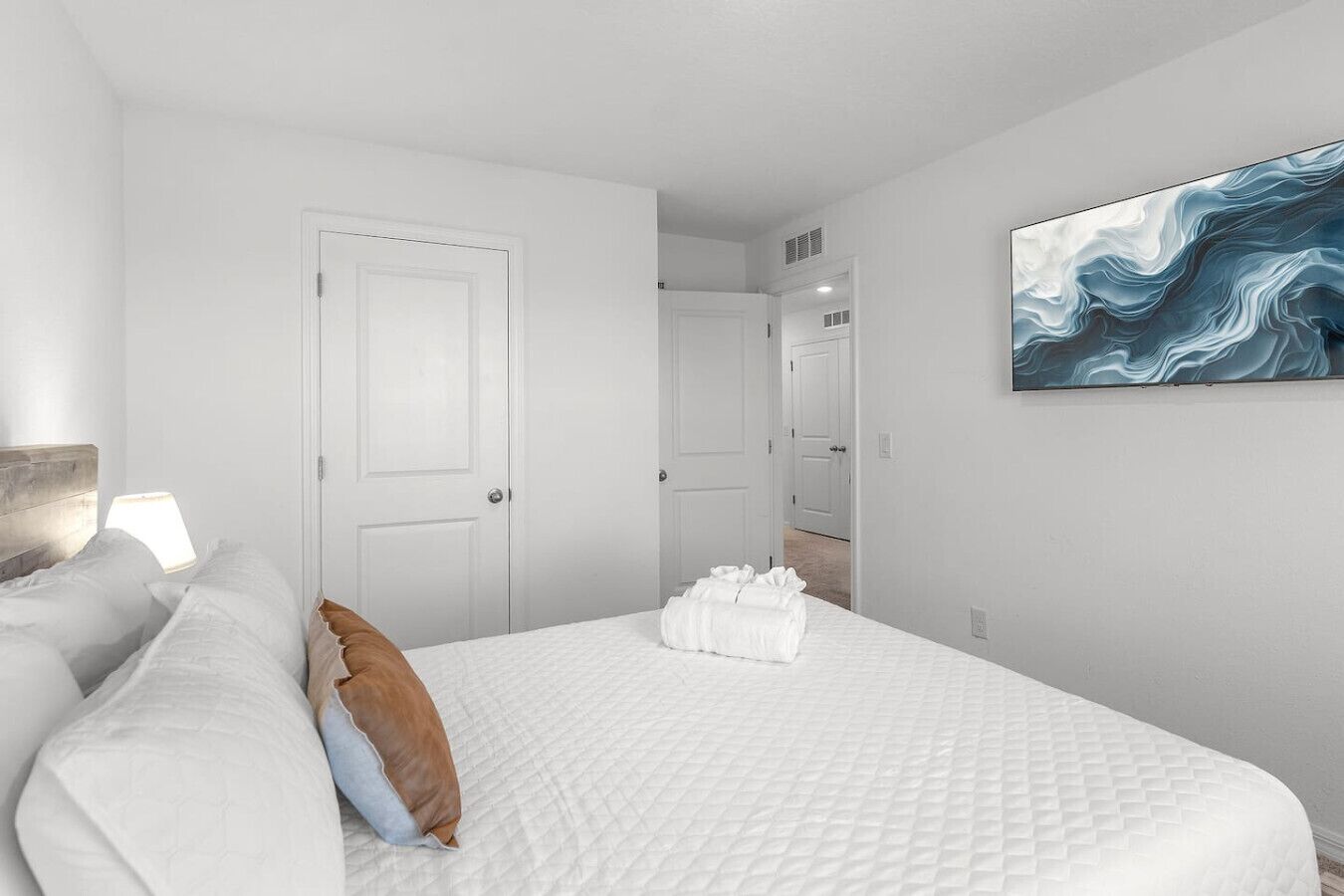 A hotel room with a large bed, white walls, a door, and a painting.
