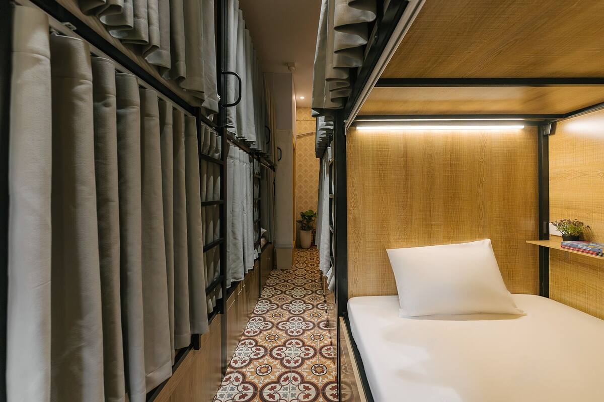 A narrow, carpeted hallway with a patterned floor leading to a bed with a white pillow and a wooden headboard.