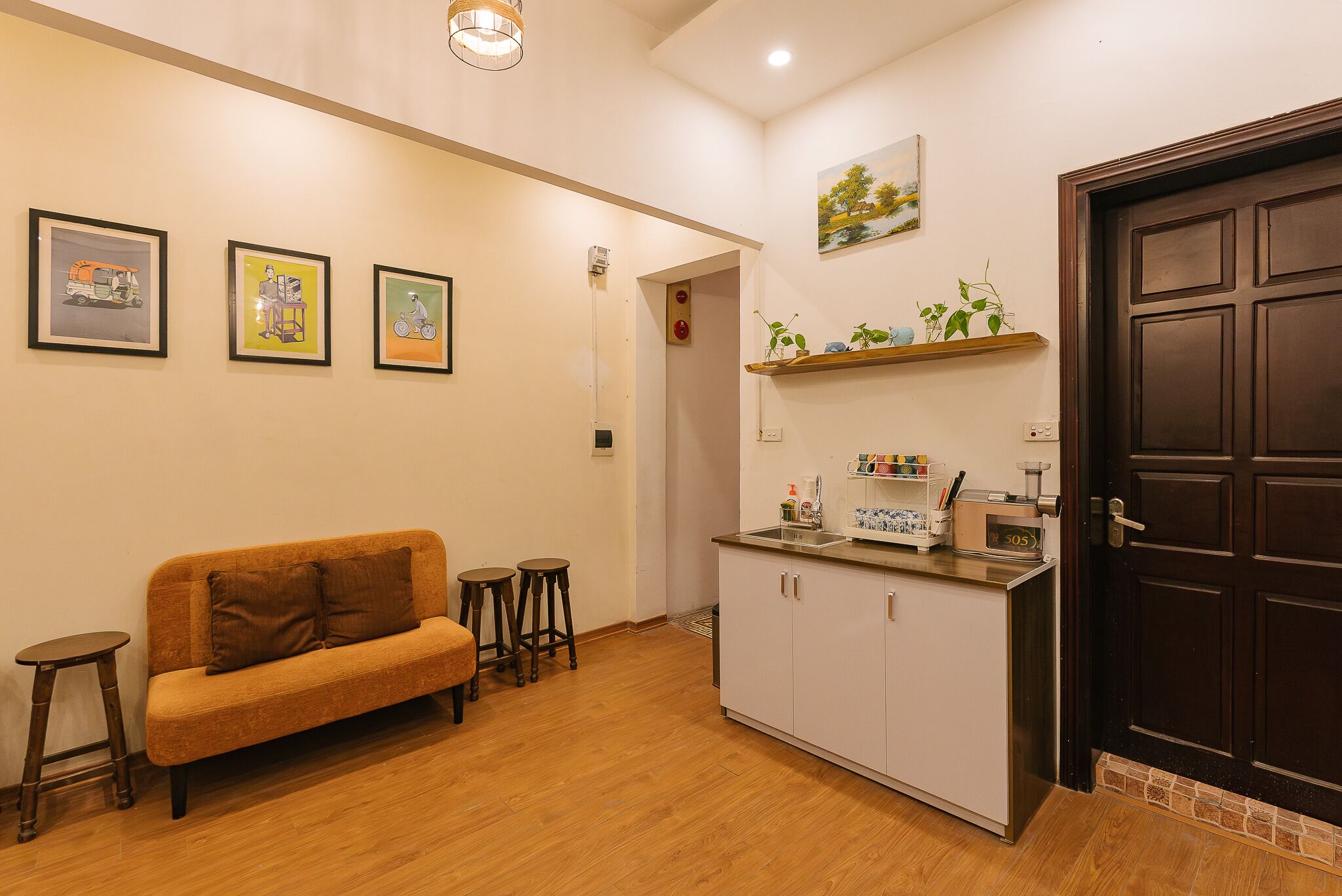 Un espacio habitable pequeño con sofá, taburetes, kitchenette y una puerta.