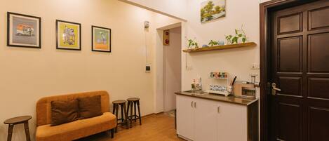 Un espacio habitable pequeño con sofá, taburetes, kitchenette y una puerta.