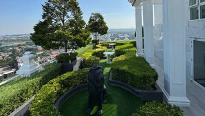 A landscaped garden with a statue, a large tree, and a view of a cityscape. - GSR-Empire Tower (Pattaya)