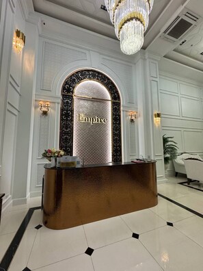 A reception desk with a gold finish, an arched doorway with the word "Empire" on it, and a chandelier above. - GSR-Empire Tower (Pattaya)